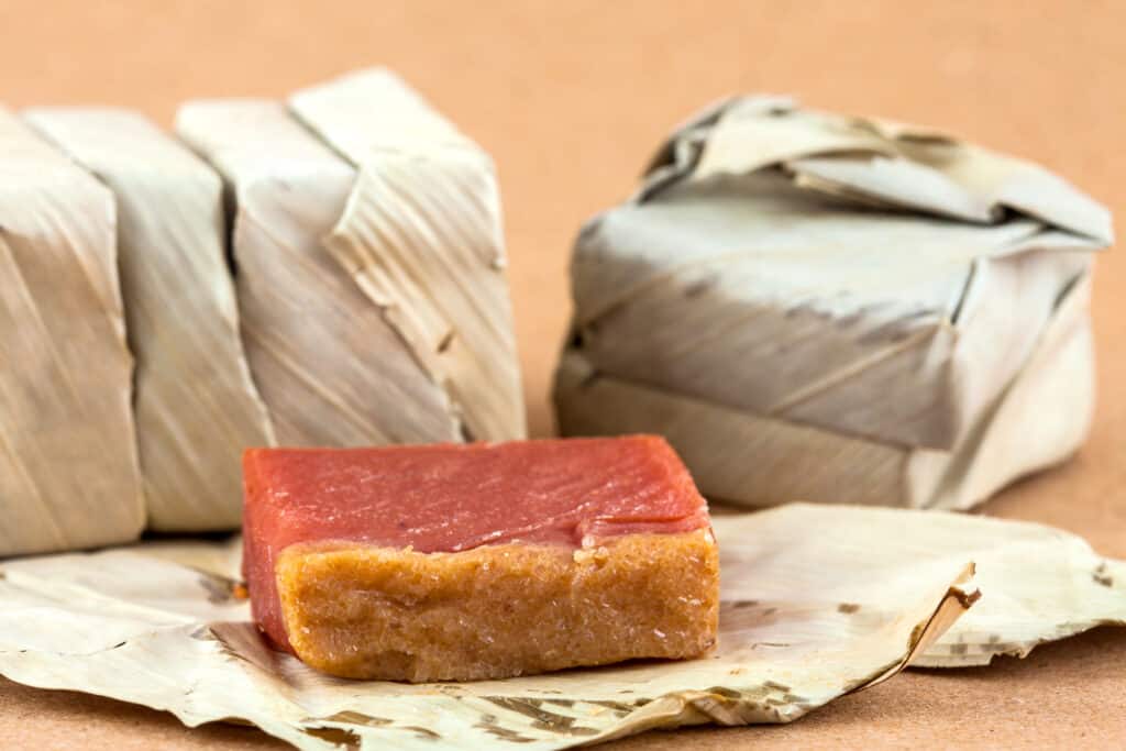 A piece of guava paste is sitting on top of a fig block wrapped in banana leaf.