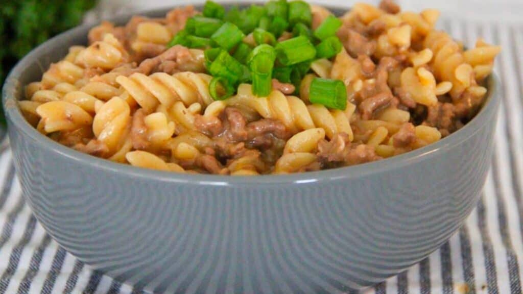 A bowl of cheesy hamburger pasta and green onions.