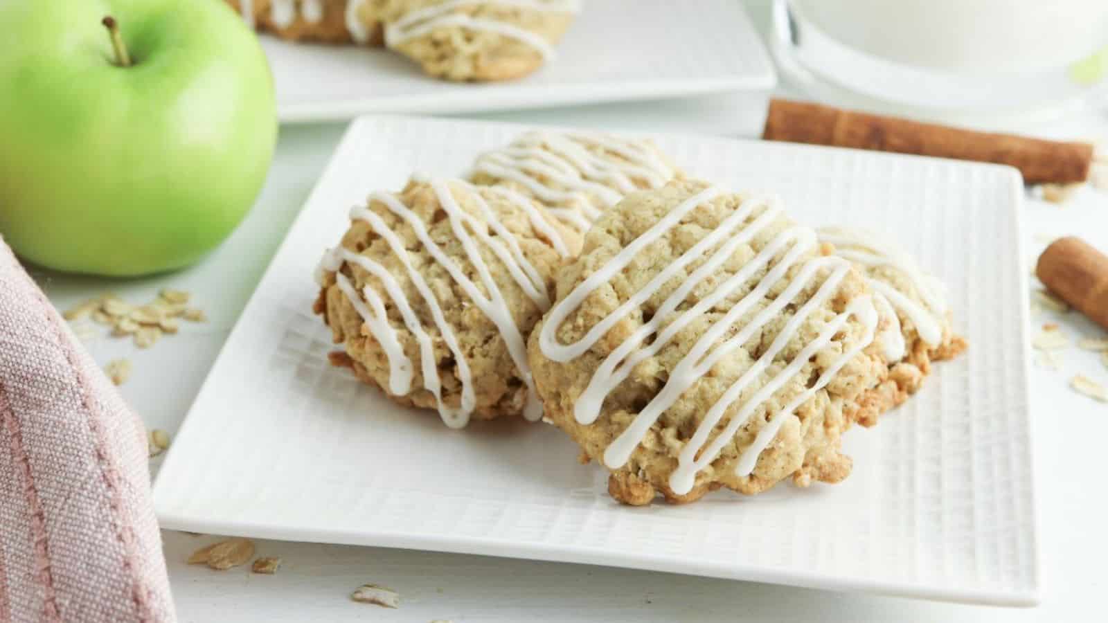 Apple oatmeal cookies with icing and apples on a white plate.