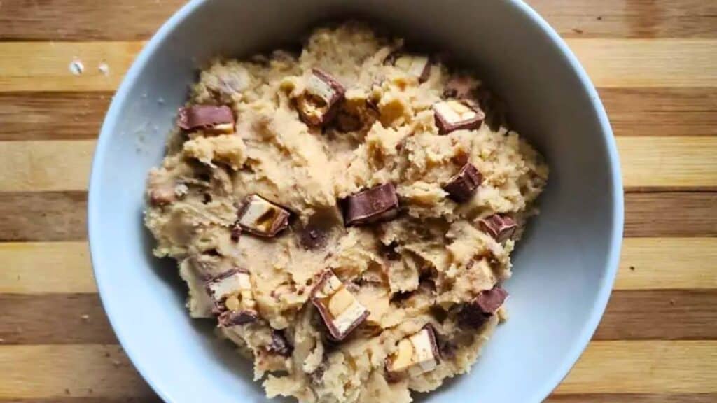 Image shows edible candy bar cookie dough in a bowl on a cutting board.