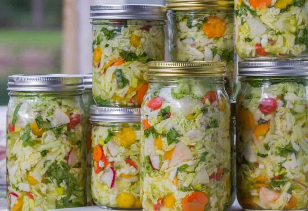 A group of jars with a variety of vegetables in them.