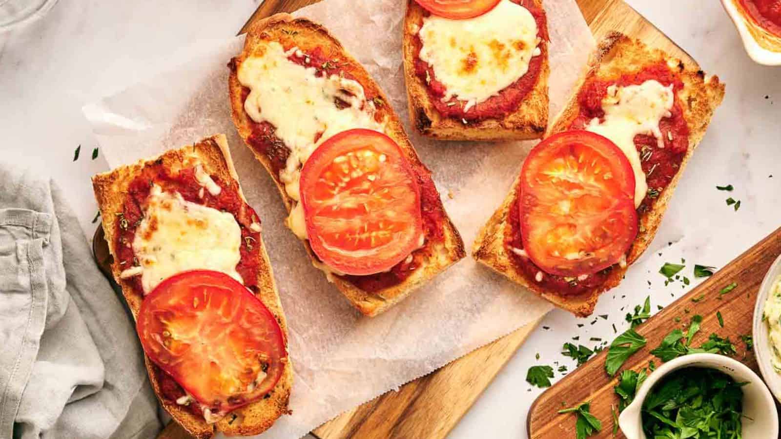 Four slices of French bread pizza with tomatoes and cheese on a cutting board.