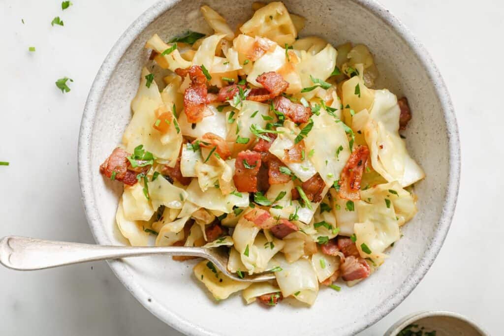 A bowl of cabbage with bacon and parsley.