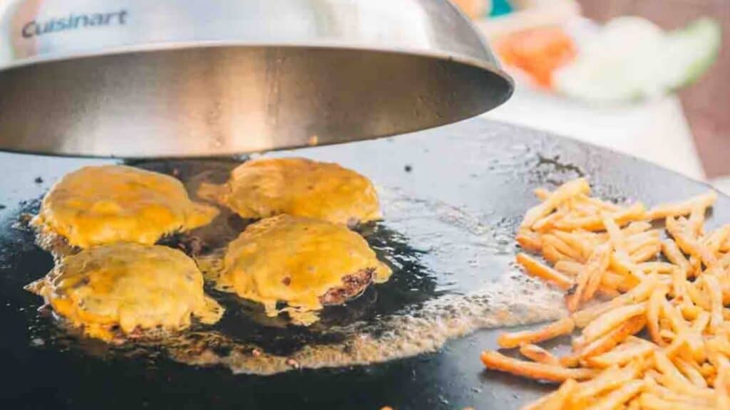 Burgers and fries are being cooked on a griddle.