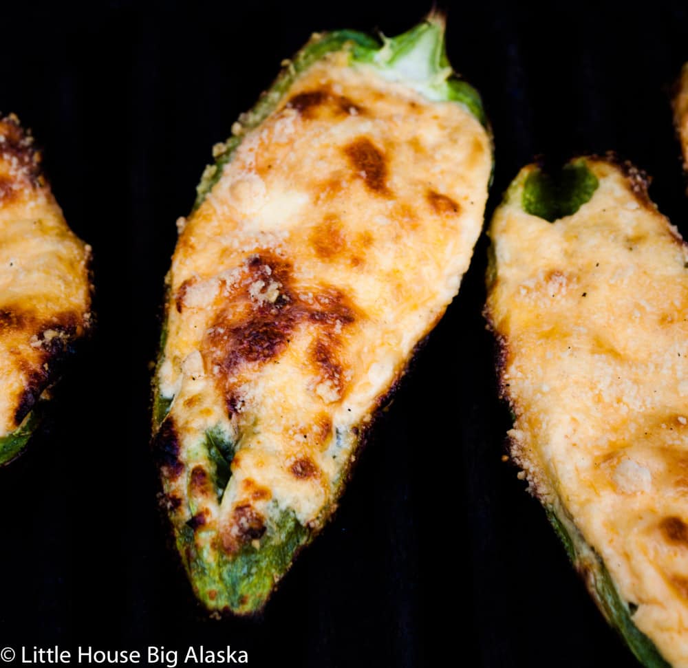 Four grilled jalapenos on a grill.