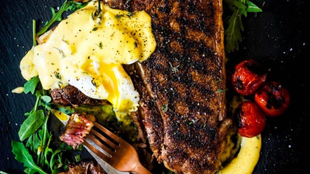 A steak with eggs and tomatoes on a plate.