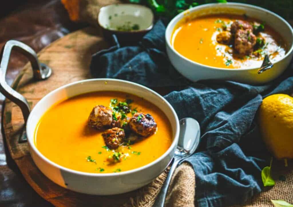 Two bowls of soup with meatballs and lemons.