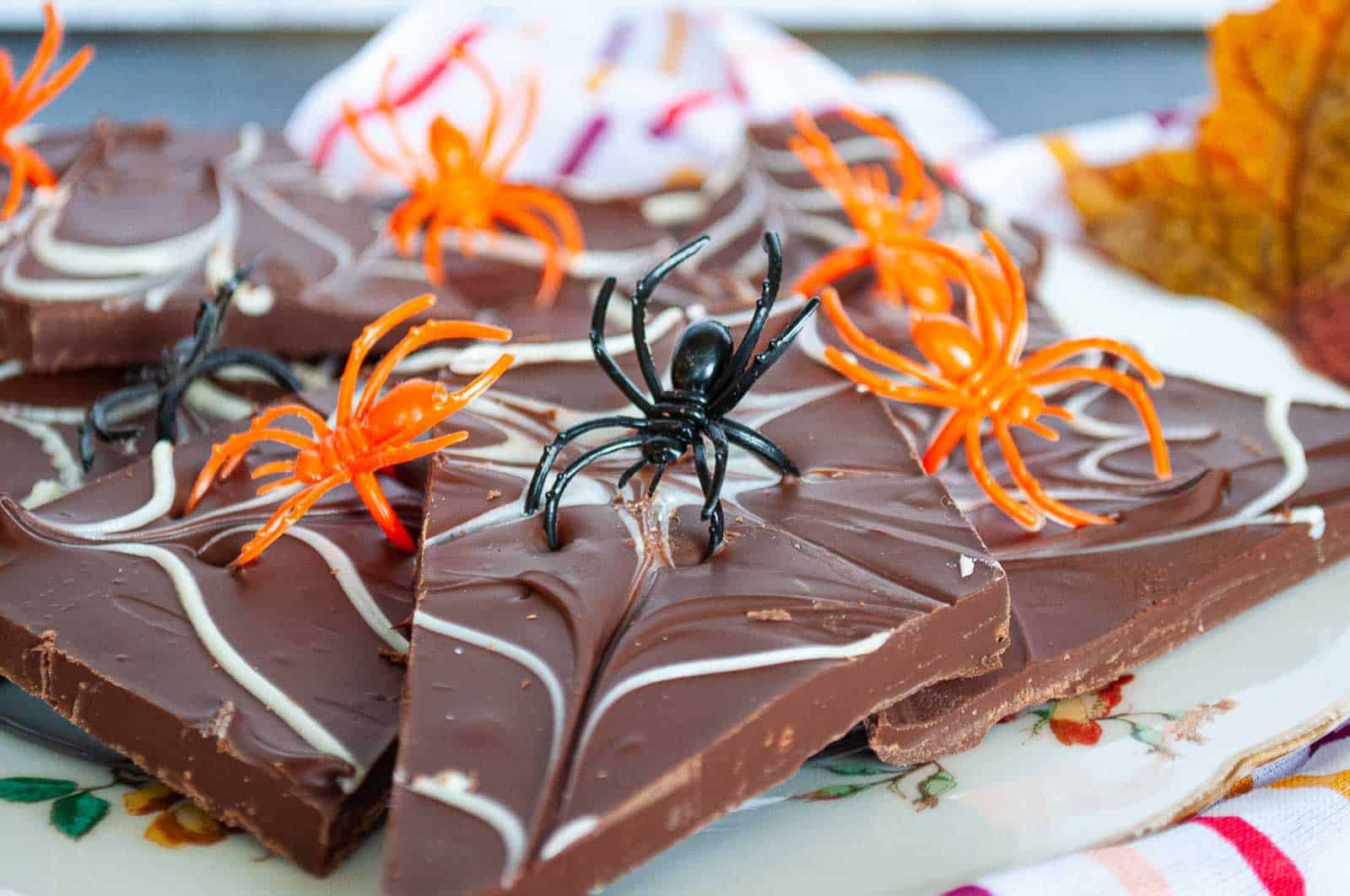A plate of chocolate bark with spider webs and plastic spiders on it.