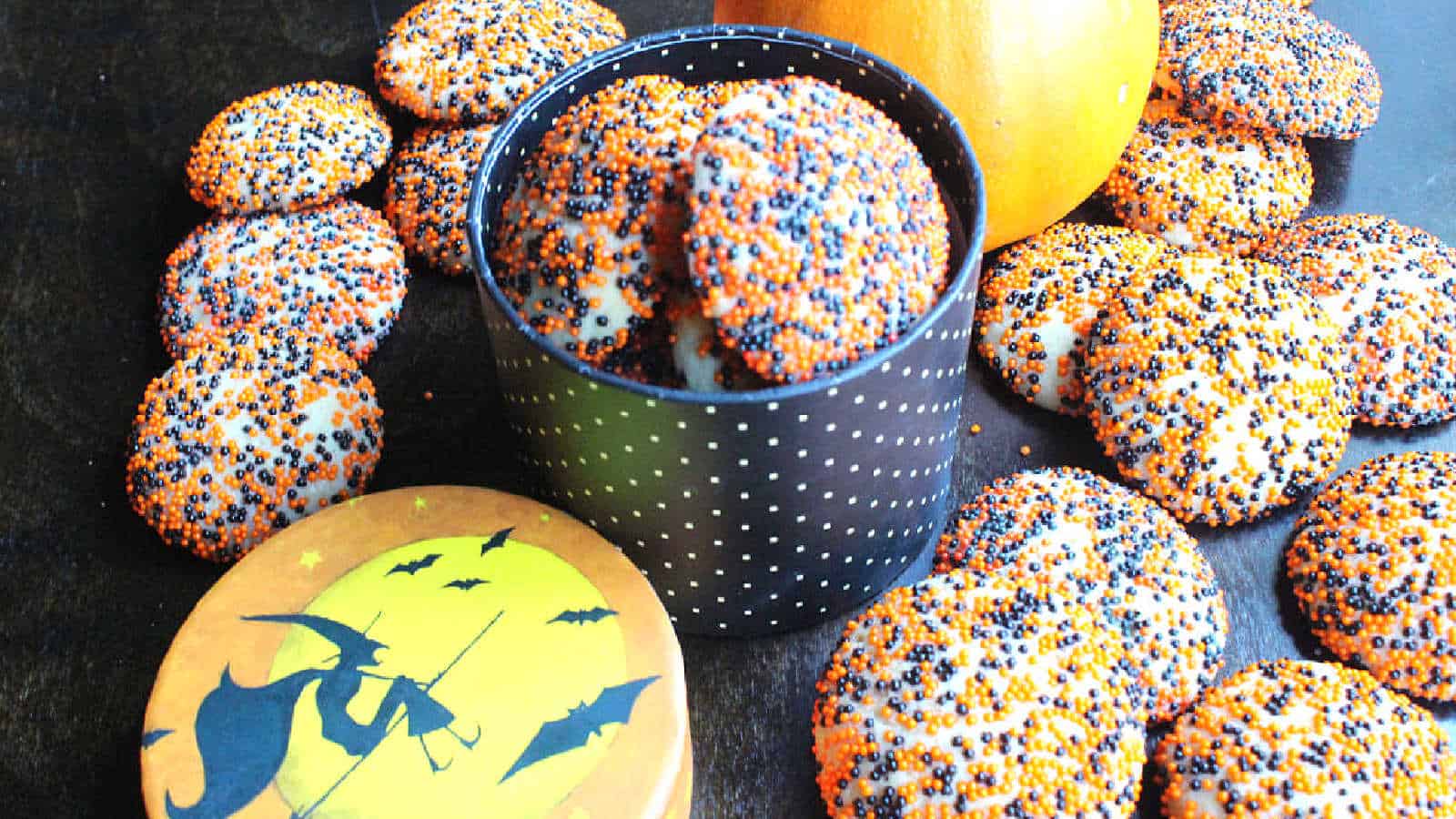 Halloween cookies with sprinkles and pumpkins on a table.