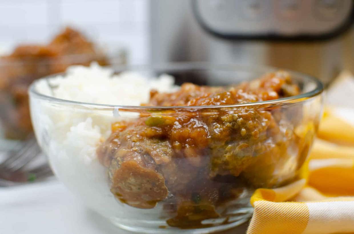 A bowl of Hawaiian meatballs with rice, spoon and fork on the side.