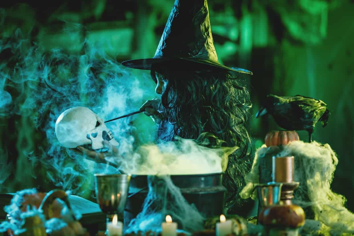 A witch is making a potion on a table at a "Hocus Pocus"-themed party.