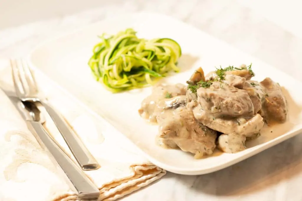 A white plate with Pork Stroganoff with Dill on it.
