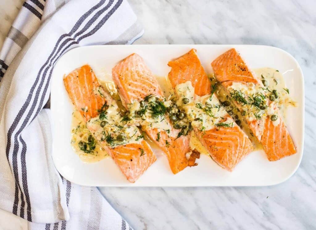 Four fillets of Salmon with Lemon Dill Cream Sauce on a white rectangular plate.