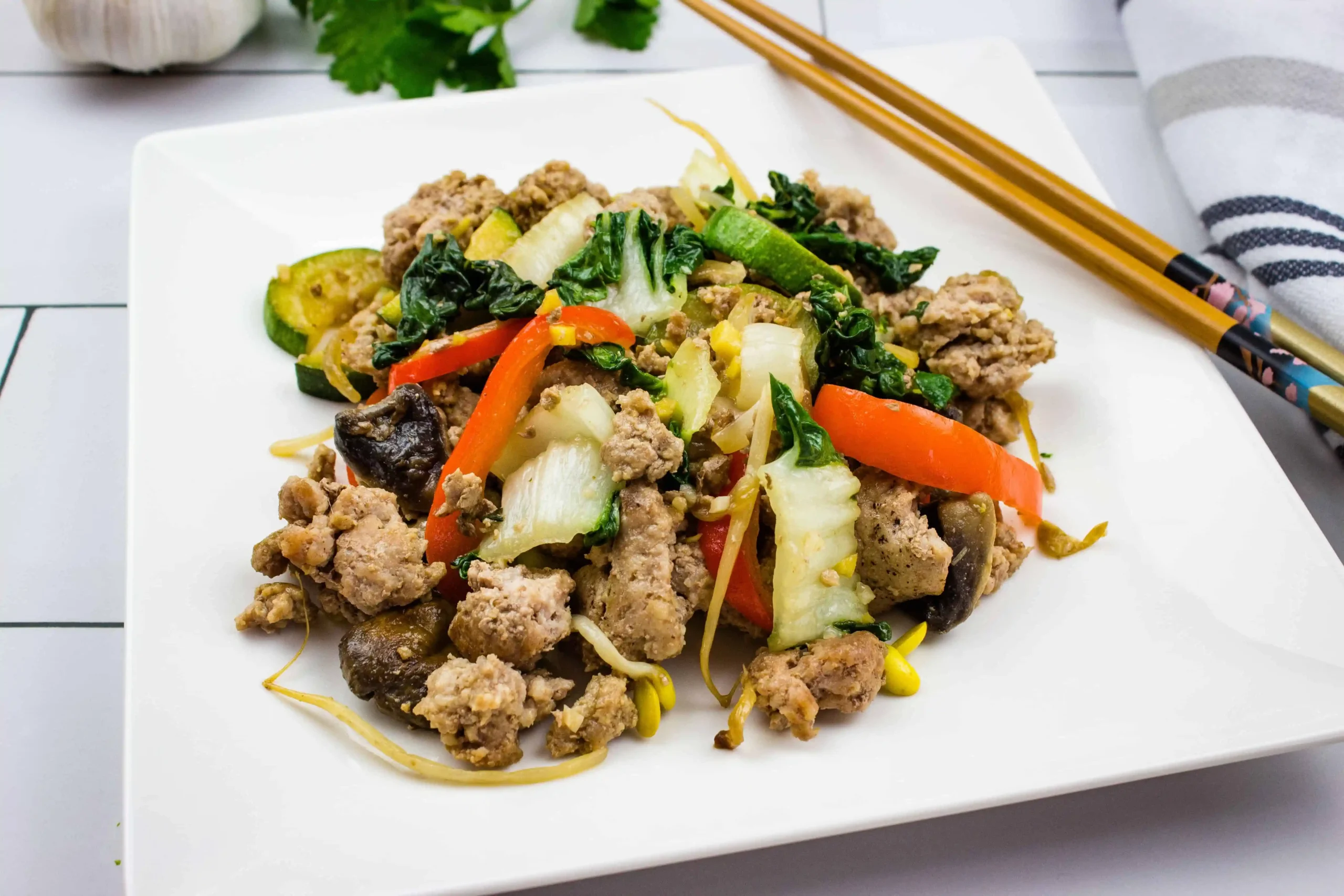 A white plate with Spicy Pork Stir Fry and chipsticks on it.