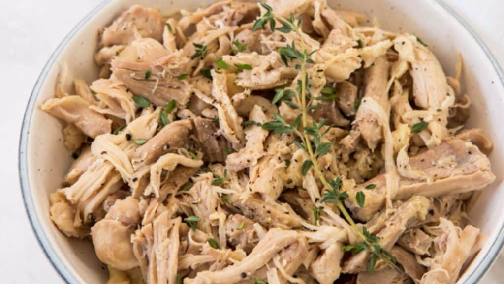 Shredded chicken in a white bowl with thyme.