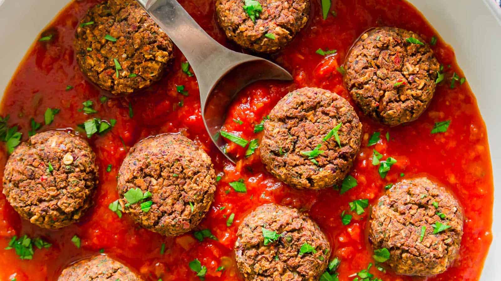 Black bean meatballs in tomato sauce with a spoon.