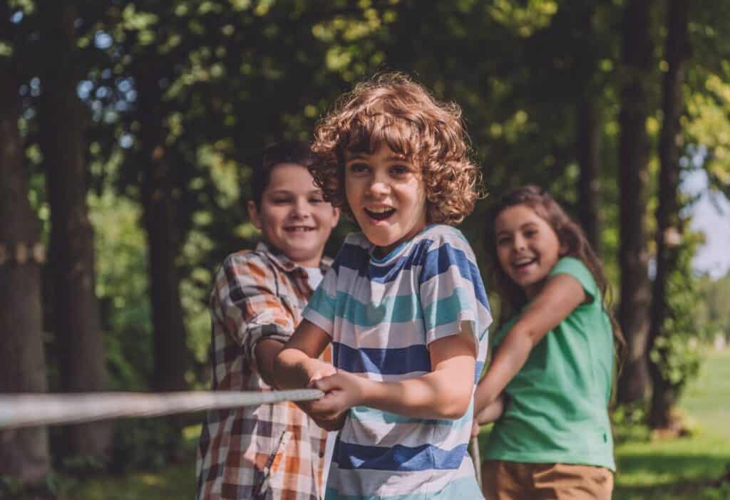 Three kids playing with a rope in a wooded area.