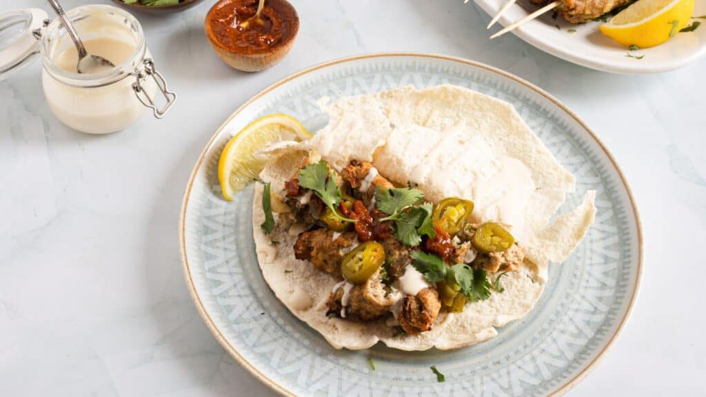 A plate with a kofta pita and skewers on it.