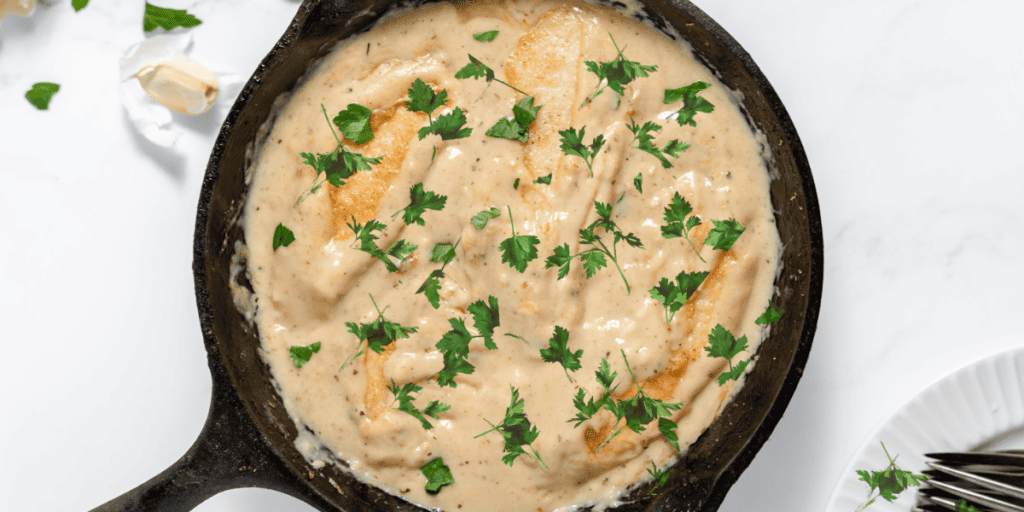 A cast iron skillet with chicken in a creamy sauce.