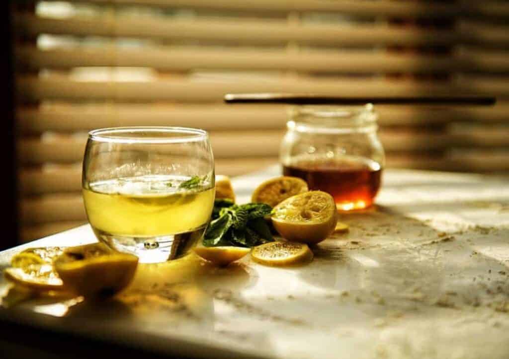A glass of lemon cocktail and a jar of honey.