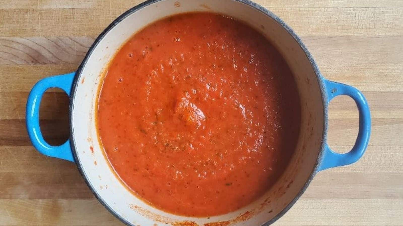 Image shows an overhead shot of a blue enameled cast iron pot with freshly made Marinara Sauce.