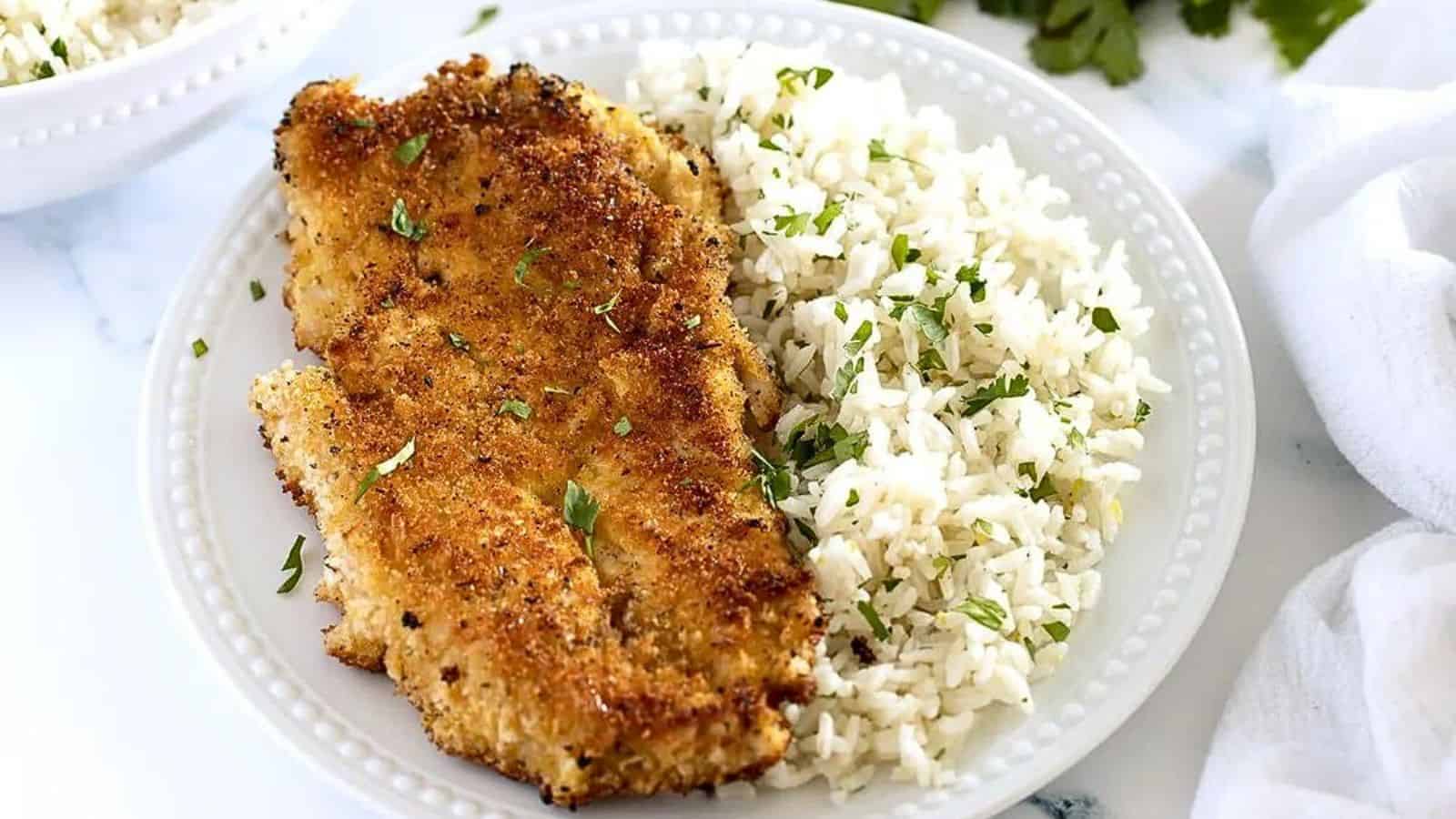 Milanesa de Pollo on a white plate with white rice and parsley flakes.