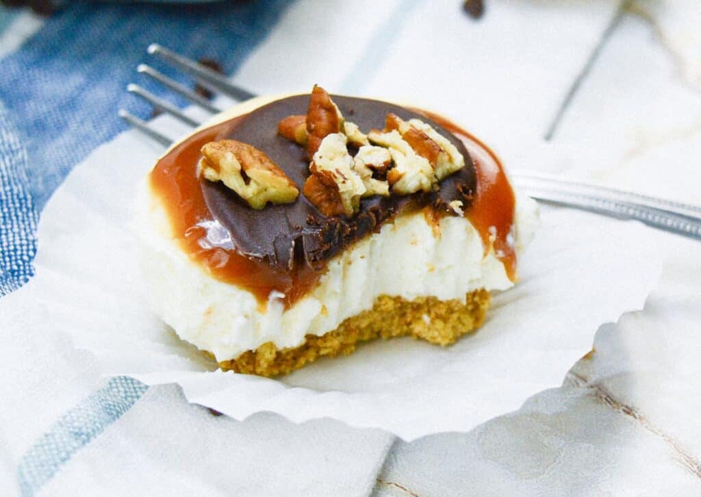 A slice of a mini turtle cheesecake with caramel and pecans on a cupcake liner.
