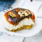 A slice of a mini turtle cheesecake with caramel and pecans on a cupcake liner.
