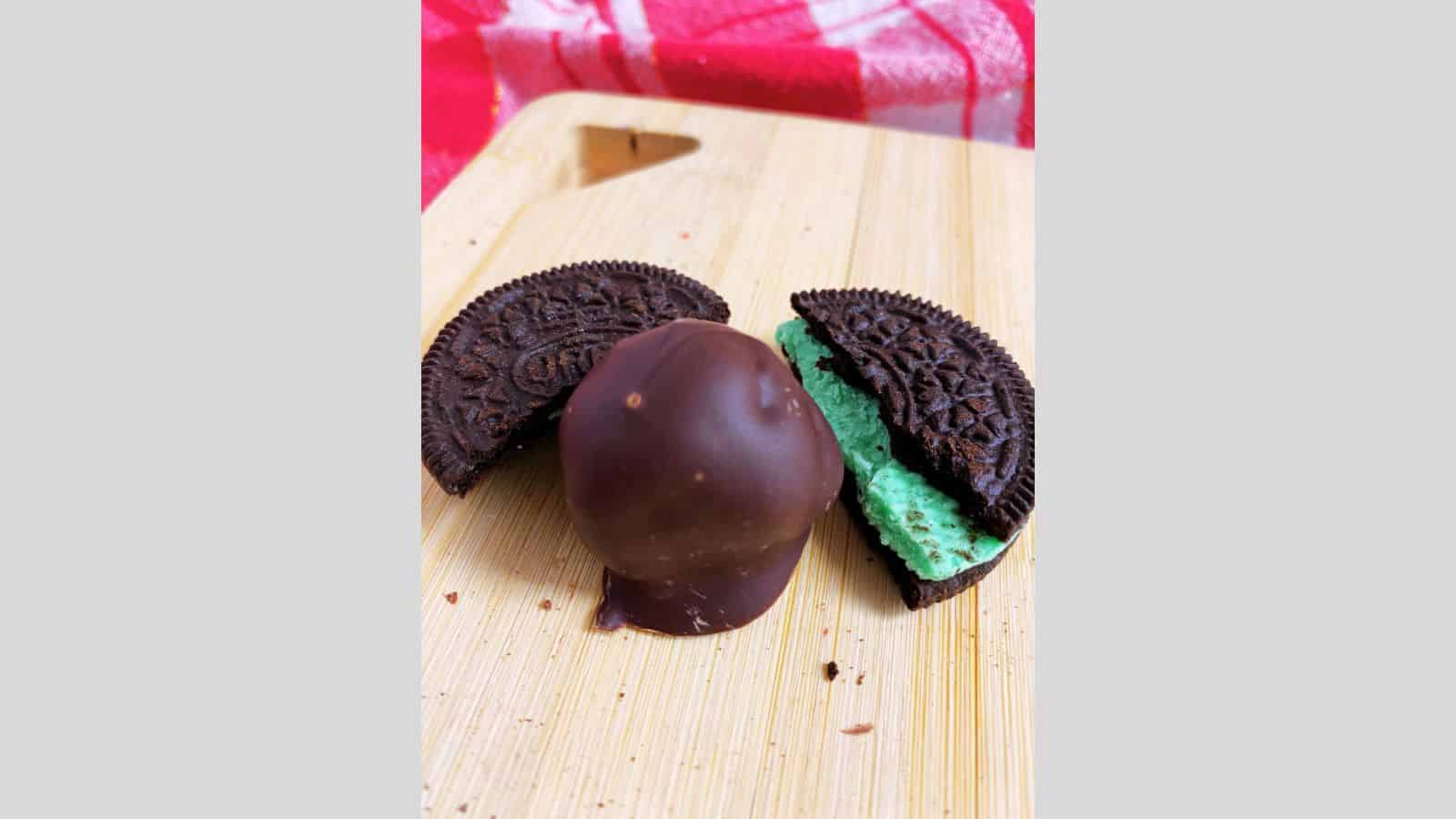 A mint truffle in the middle of a broken mint Oreo cookie with green icing.
