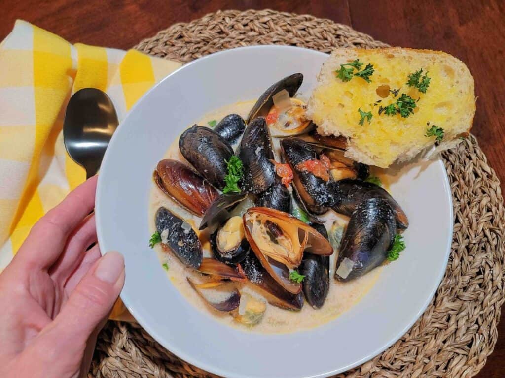 A bowl of mussels in cream sauce with a side of garlic bread