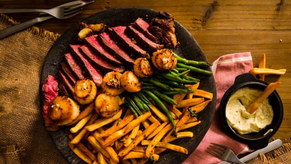 A plate with steak, scallops and green beans on a wooden table.