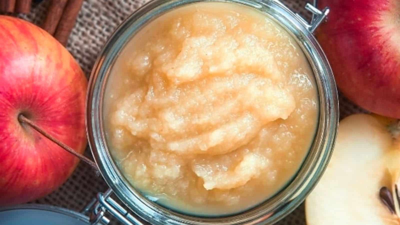 A jar of apple sauce next to apples and cinnamon.