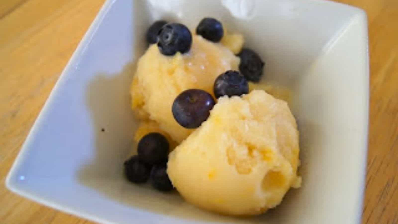 Image shows scoops of Peach Coconut Milk Ice Cream in a white bowl with blueberries.