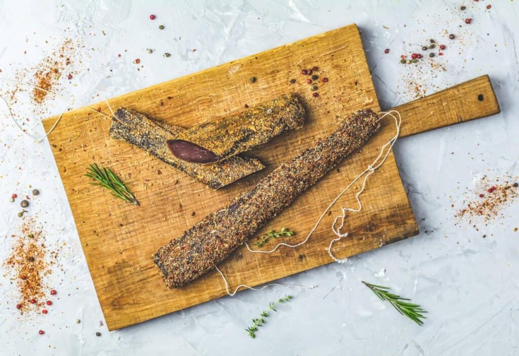 A piece of meat on a cutting board with herbs and spices.