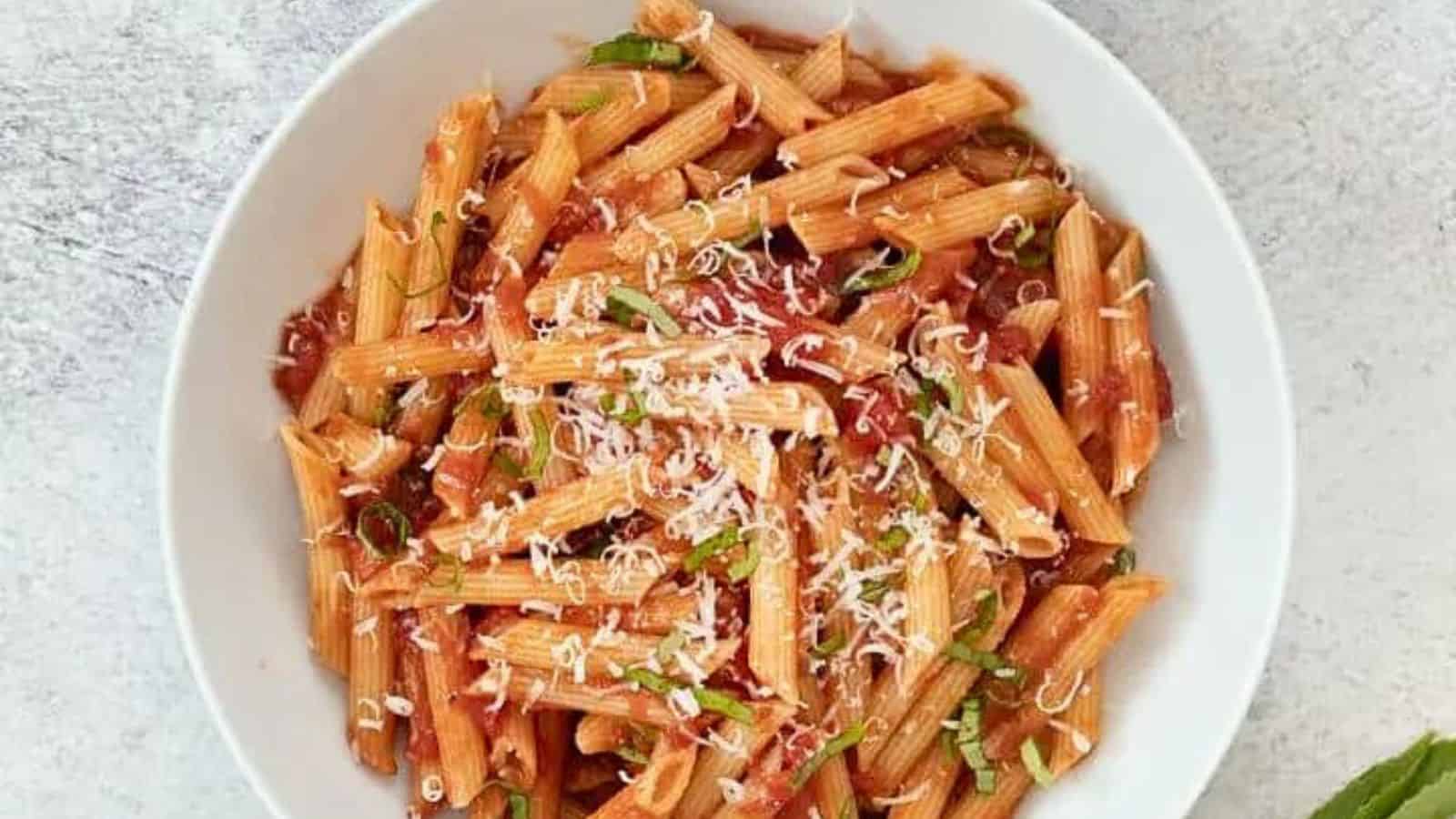 Penne pomodoro in a white bowl surrounded by fresh basil.