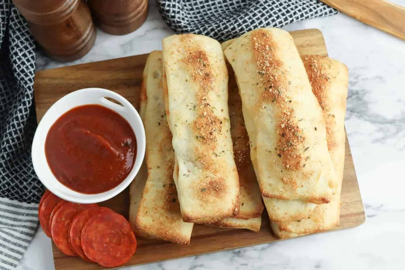Breadsticks on a wooden server with pepperonis and marinara sauce.