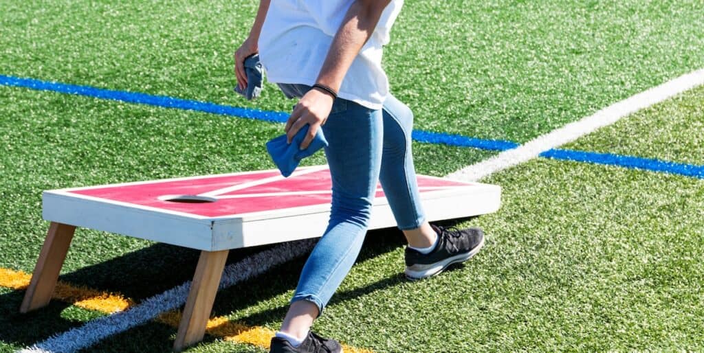 A person getting ready to toss a cornhole bean bag while standing next to board.