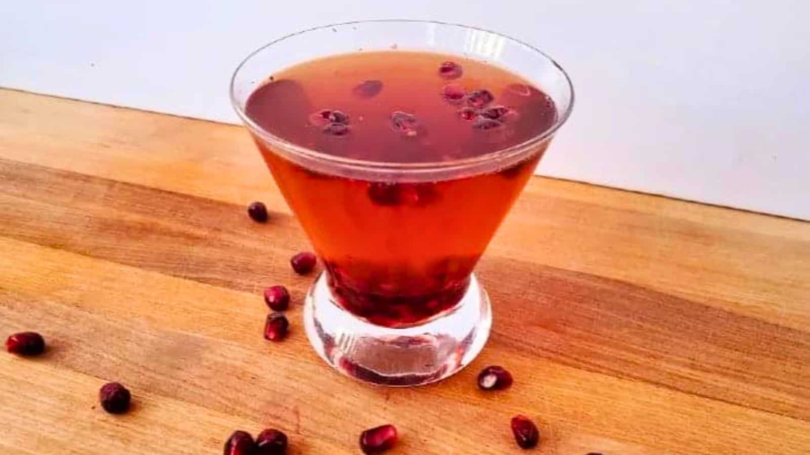 Image shows a martini glass with a Pomegranate Fizz Cocktail and pomegranate arils around it.