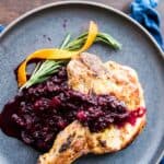 Pork chops with blackberry applesauce on a gray plate.