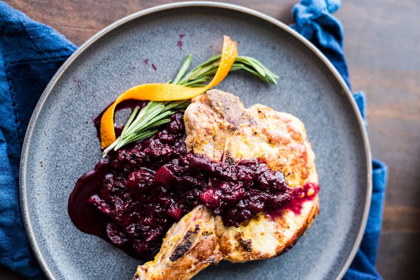 Pork chops with blackberry applesauce on a gray plate.