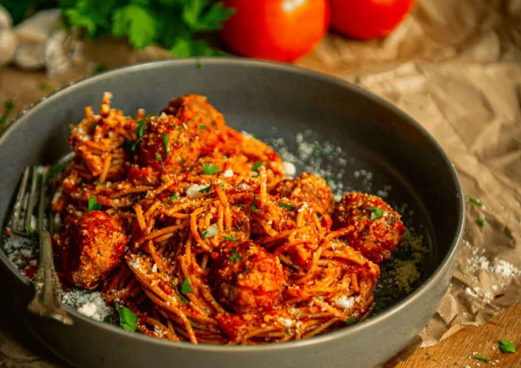 A bowl of spaghetti with meatballs and tomatoes.