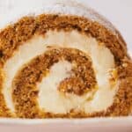 A slice of pumpkin roll being sprinkled with powdered sugar.