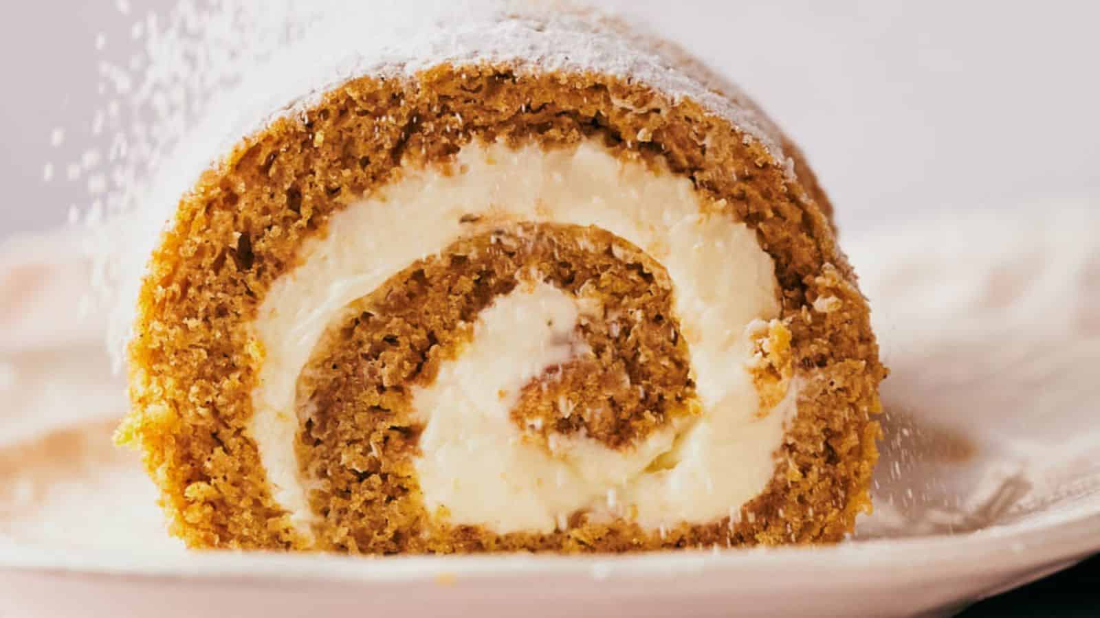 A slice of pumpkin roll being sprinkled with powdered sugar.