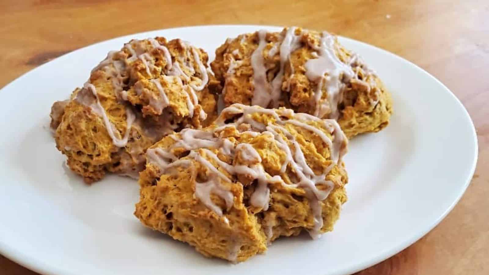 Image shows Three pumpkin scones on a plate with icing.