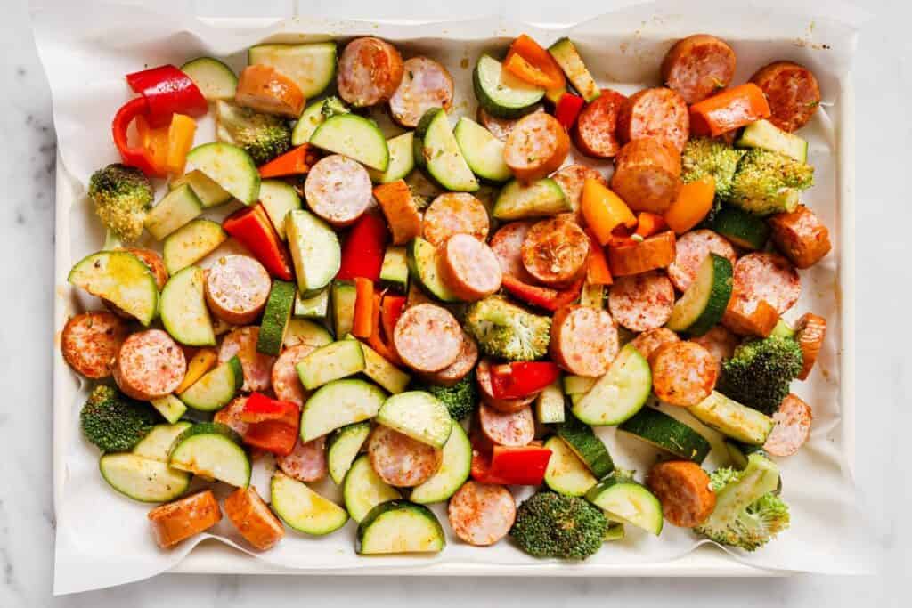 A baking sheet with vegetables and sausages.