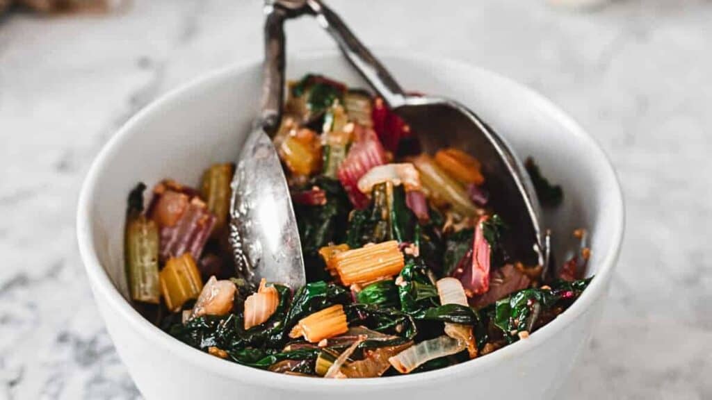 Side view of white bean salad in bowl with tongs.