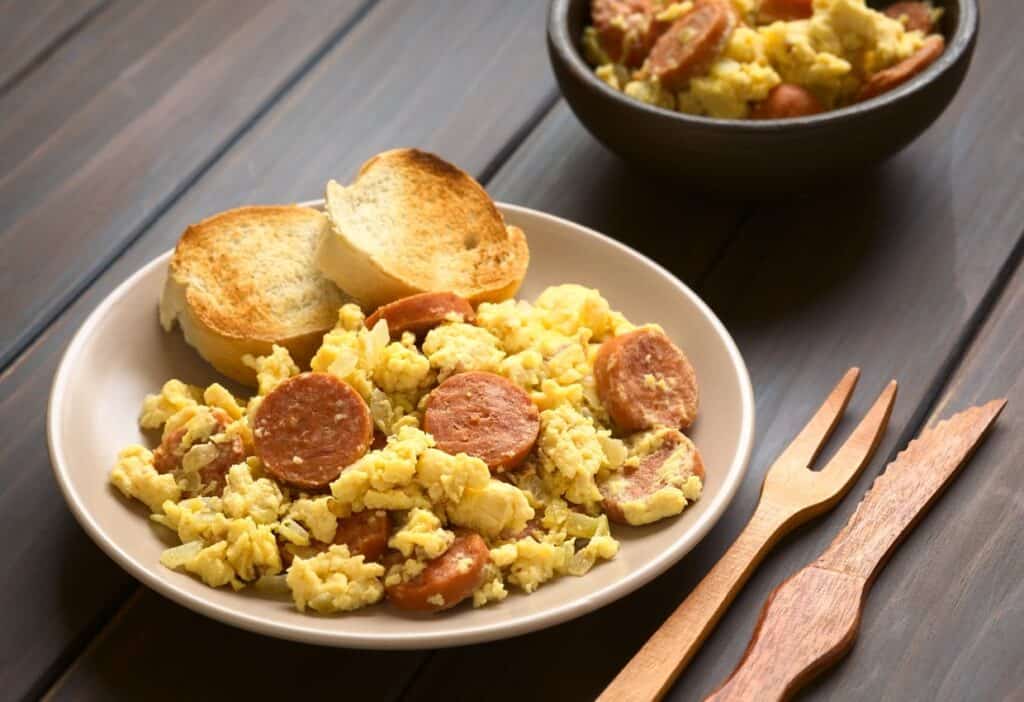 Scrambled eggs with chorizo and toast on a wooden table.
