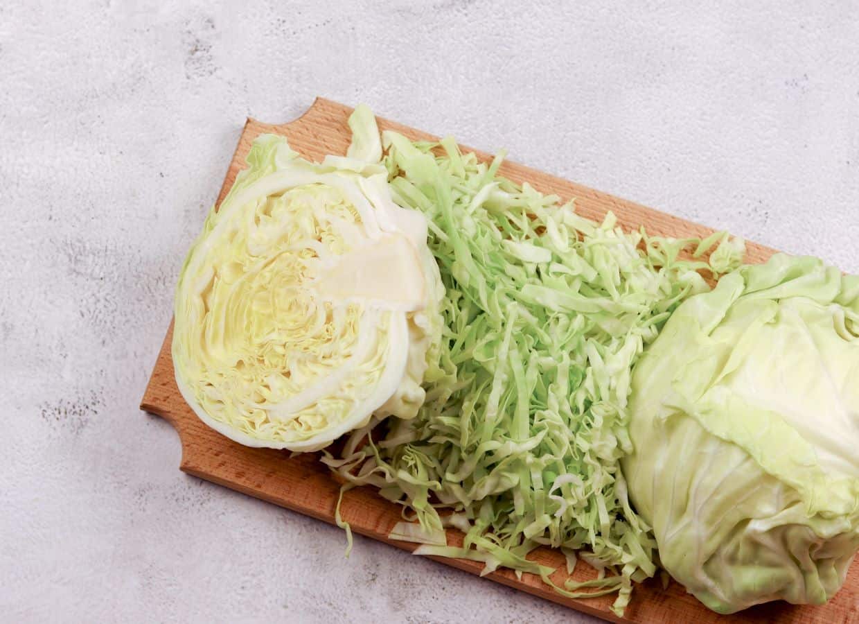 Cabbage cut in half with shredded cabbage on a cutting board.