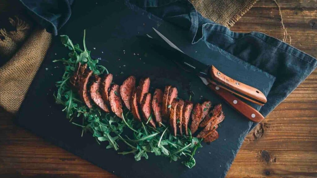 Steak on a cutting board with a knife and arugula.
