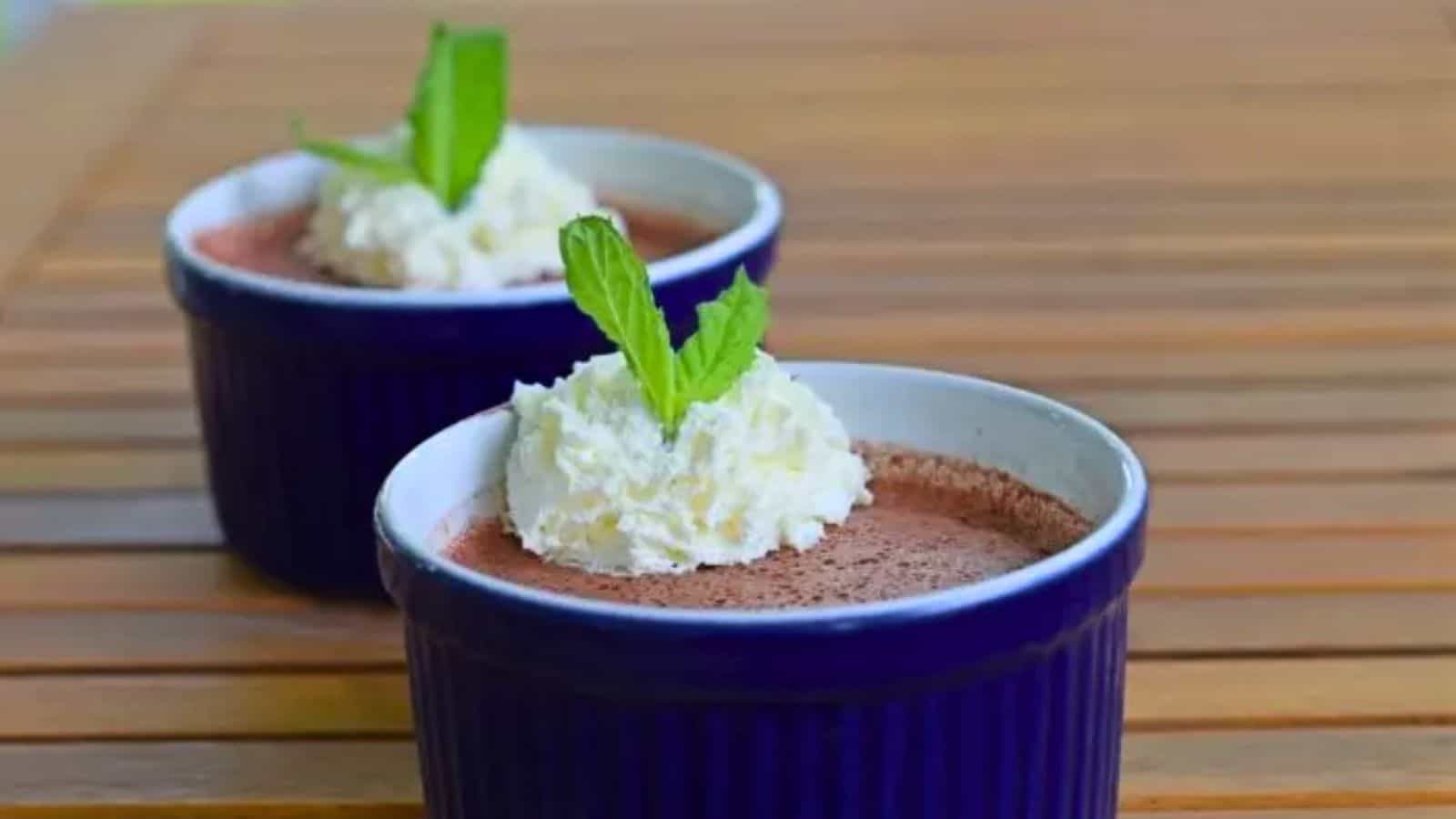 Image shows two ramekins with Cherry Custard in blue ramekins topped with whipped cream and mint leaves.